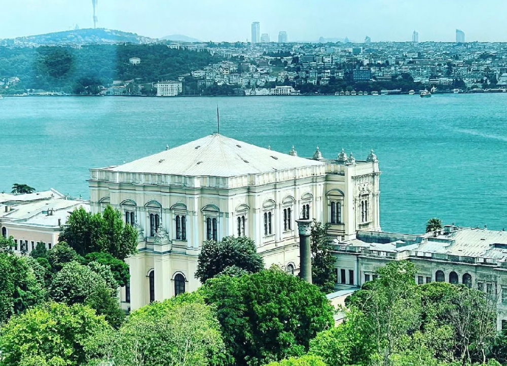 İstanbul Boğazı kıyısındaki tarihi yapı, yeşillikler ve karşı yakadaki şehir manzarası.